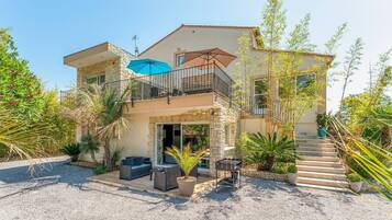A two-story house with a balcony, outdoor seating, and a barbecue area.