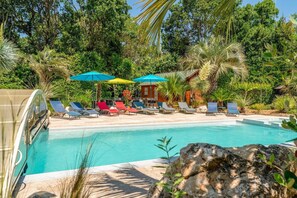 Ein Poolbereich mit Liegestühlen und Sonnenschirmen, umgeben von üppiger Vegetation und einer Holzkonstruktion.