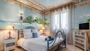 Une chambre à coucher avec un lit, des tables de chevet, un téléviseur et une fresque murale représentant une plage.