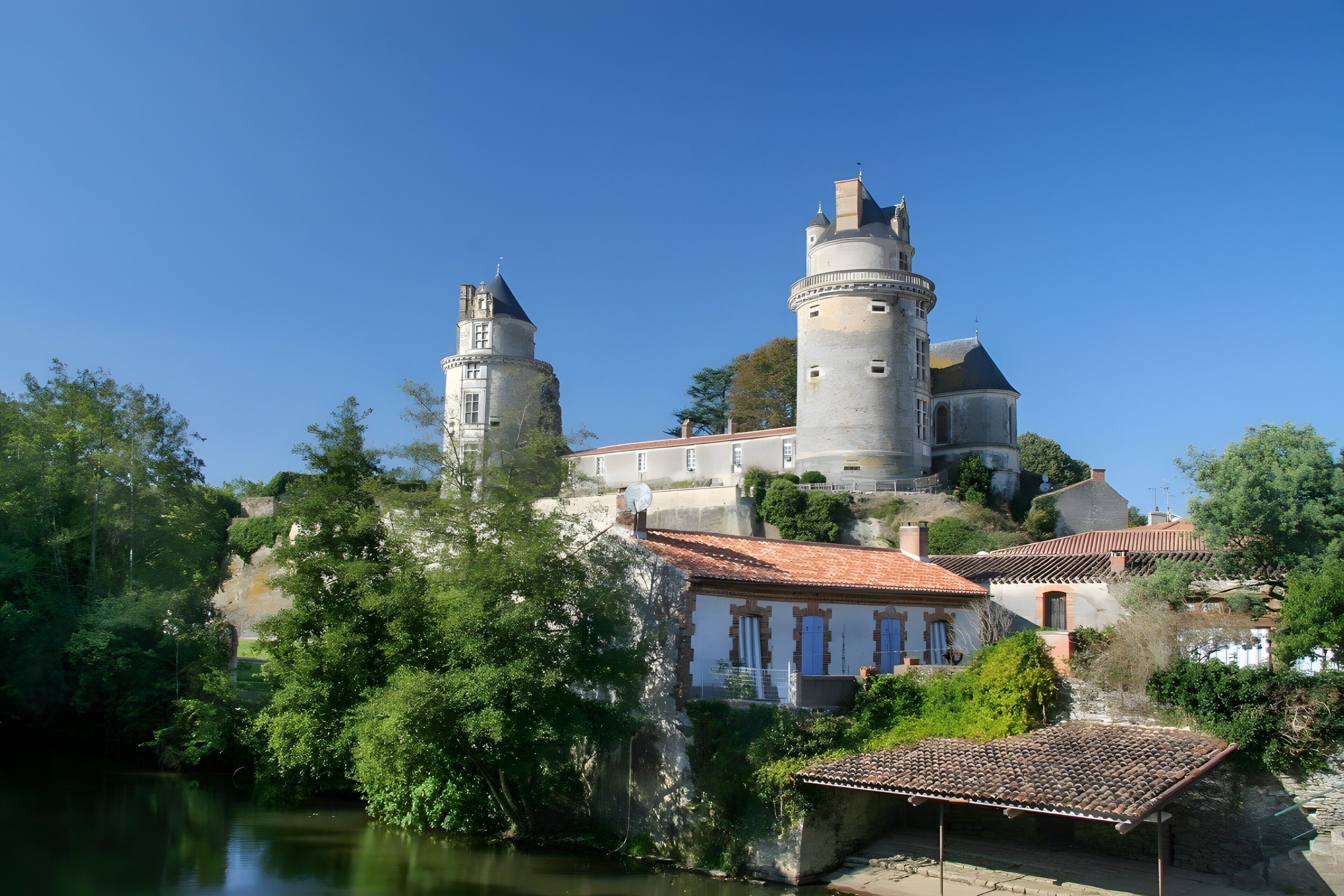 A castle with two towers, a river, and surrounding greenery.