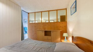 Quarto com cama, guarda-roupa de madeira e mesa de cabeceira com abajur.