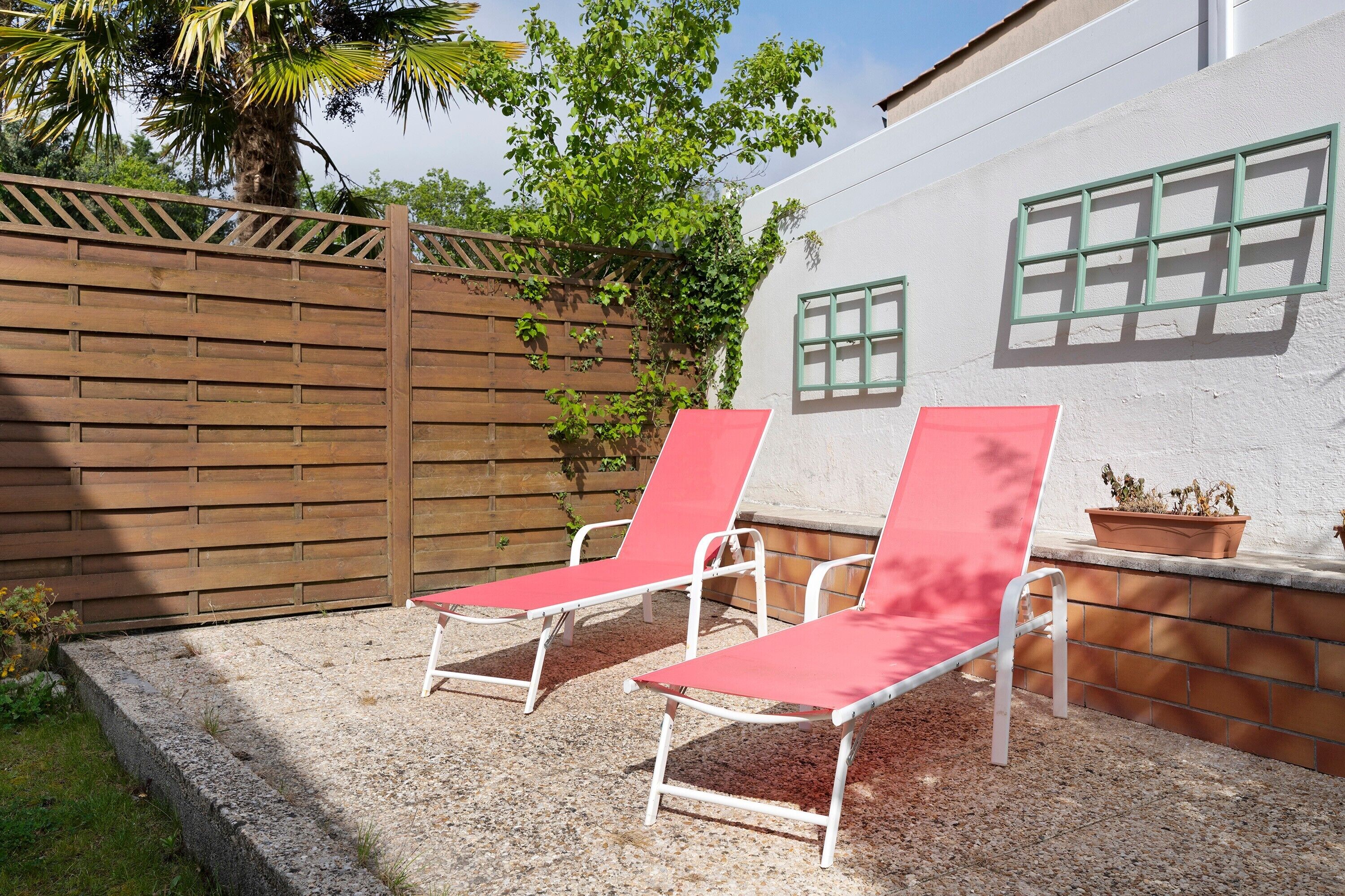 Two red lounge chairs, a wooden fence, and a white wall with windows.