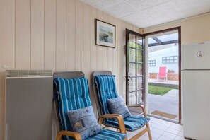 Une pièce comprenant deux fauteuils, un radiateur fixé au mur, une porte donnant sur l’extérieur et un réfrigérateur blanc.