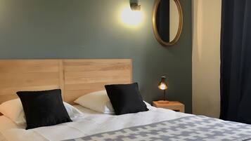 A neatly made bed with a patterned blanket, a wooden headboard, a round mirror, and a wall-mounted light fixture.