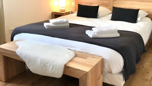 Un lit double avec une tête de lit en bois, deux tables de chevet avec des lampes, un banc et un luminaire fixé au mur.