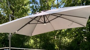 Une terrasse extérieure avec une table et des chaises, un grand parasol et une vue sur un paysage verdoyant.