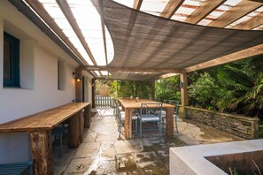 Eine Terrasse im Freien mit Holztisch und -stühlen, umgeben von Steinböden und einer Holzpergola.