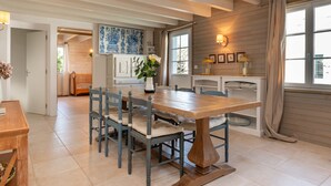 Un comedor con mesa y sillas de madera, un jarrón con flores y vistas al exterior.