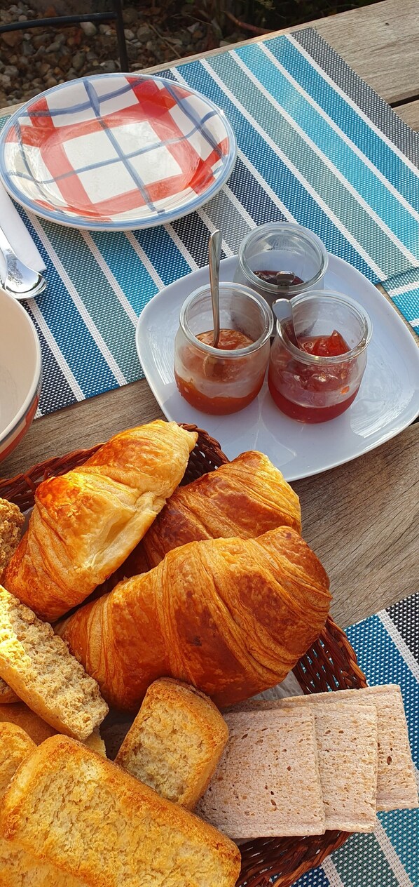 Un montaje para picnic con cruasanes, pan y mermelada sobre un mantel a rayas.