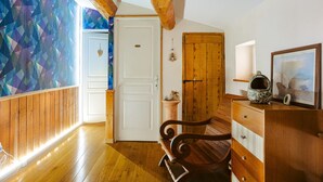 A room with wooden floors, a bench, a wooden dresser, a door, and a wall with geometric patterns. - Guest Rooms - Aubépine and Bleuet Rooms (Courçon)