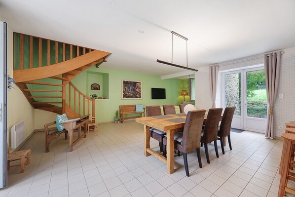 Un coin repas avec une table et des chaises en bois, un escalier et une vue à travers une porte vitrée.