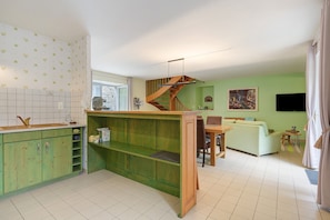 Une cuisine avec un îlot central en bois, un coin repas avec un canapé et un escalier.