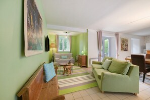A living room with a sofa, a wooden bench, a small table, and a lamp. - Domaine de la Dauvinerie – Escapade Cottage (Gratot)