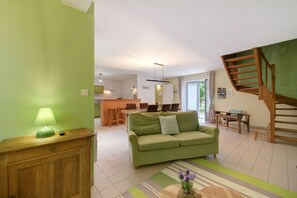 Un salon avec un canapé vert, un meuble en bois, une lampe et un escalier.