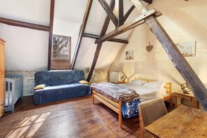 Un dormitorio acogedor en el desván con techo inclinado, cama de madera, sofá azul, una mesita y una cuna.