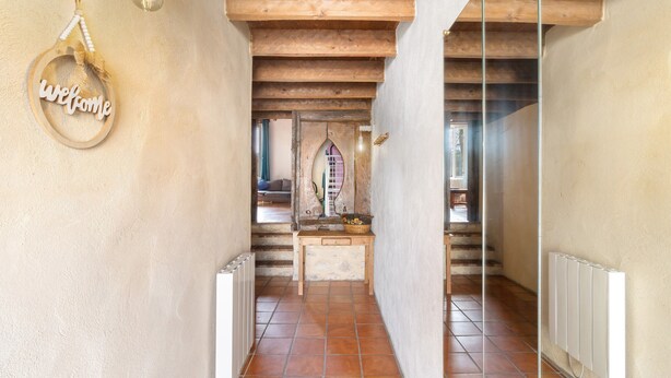 A hallway with a wooden ceiling, a welcome sign, a small table with a basket, and a view into another room.