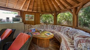 A covered outdoor seating area with a wooden ceiling, wicker furniture, and a round table with books and a coffee pot. - Bed and Breakfast 'Espace Roulotte - Les Toits Du Gaou' with Shared Terrace and Wi-Fi (Six-Fours-les-Plages)