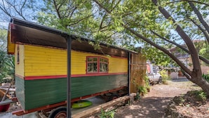 A colorful, stationary house with a window and a door, surrounded by trees and a vehicle in the background. - Bed and Breakfast 'Espace Roulotte - Les Toits Du Gaou' with Shared Terrace and Wi-Fi (Six-Fours-les-Plages)