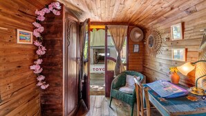 A wooden cabin interior with a bed, a chair, a table with a lamp, and a door leading outside. - Bed and Breakfast 'Espace Roulotte - Les Toits Du Gaou' with Shared Terrace and Wi-Fi (Six-Fours-les-Plages)