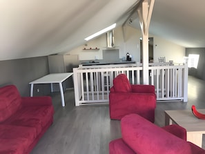 A modern loft with a kitchen, a dining area, and red sofas.