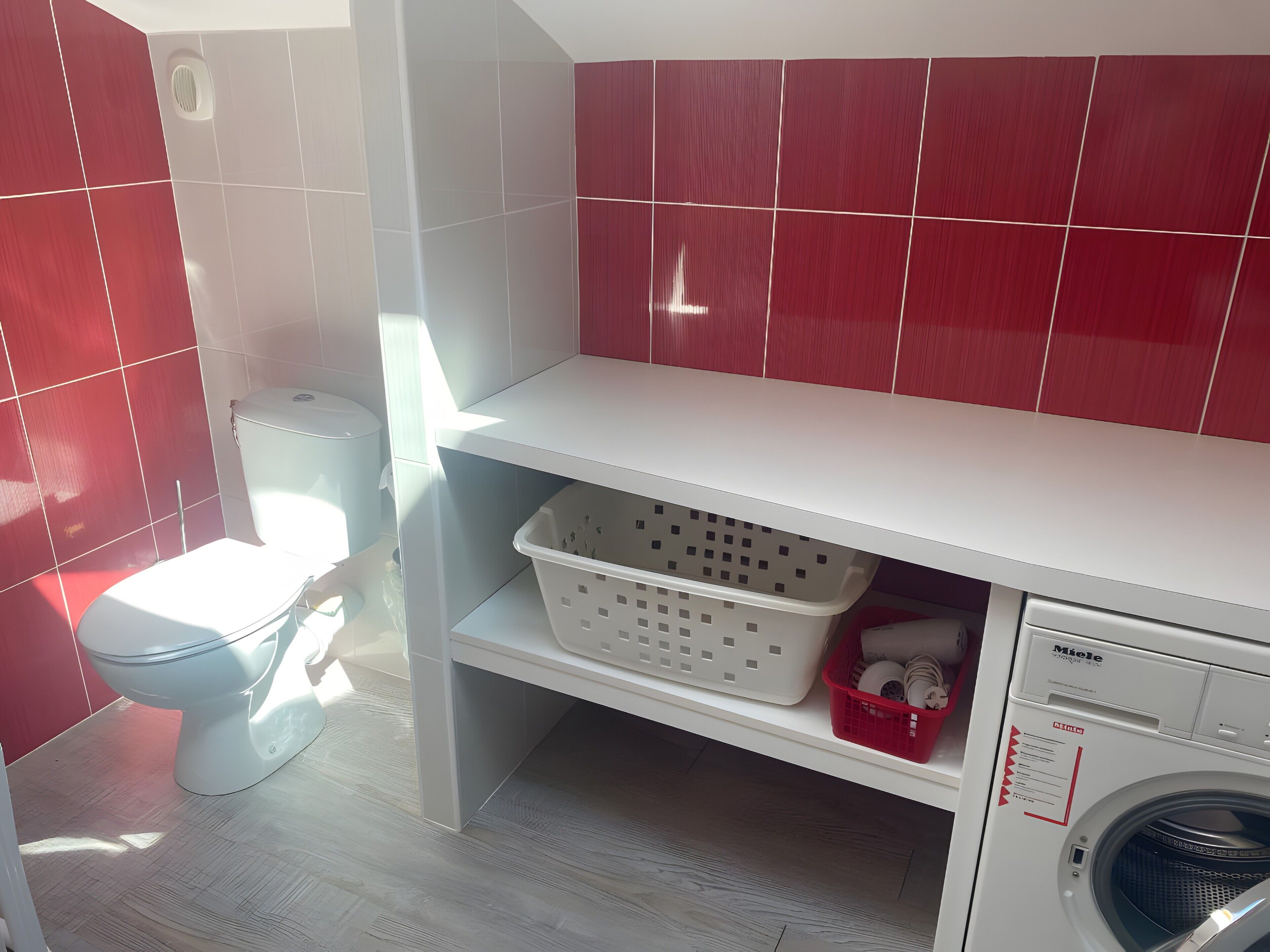 Un bagno con un water, una lavatrice e uno scaffale con cesti per la biancheria.