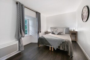 Ein Schlafzimmer mit Bett, Nachttisch, einem Fenster mit Vorhängen und einem Wandbild.