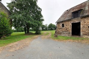 Een landelijke omgeving met een stenen gebouw, een onverharde weg en een grote boom.
