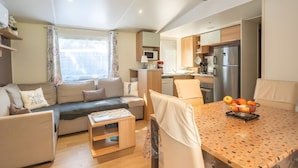 A modern living room with a sofa, a coffee table, and a dining area with a table and chairs. - Mobile Home 'Mh324 La Tremblade' with Shared Pool, Private Terrace, and Air Conditioning (La Tremblade)