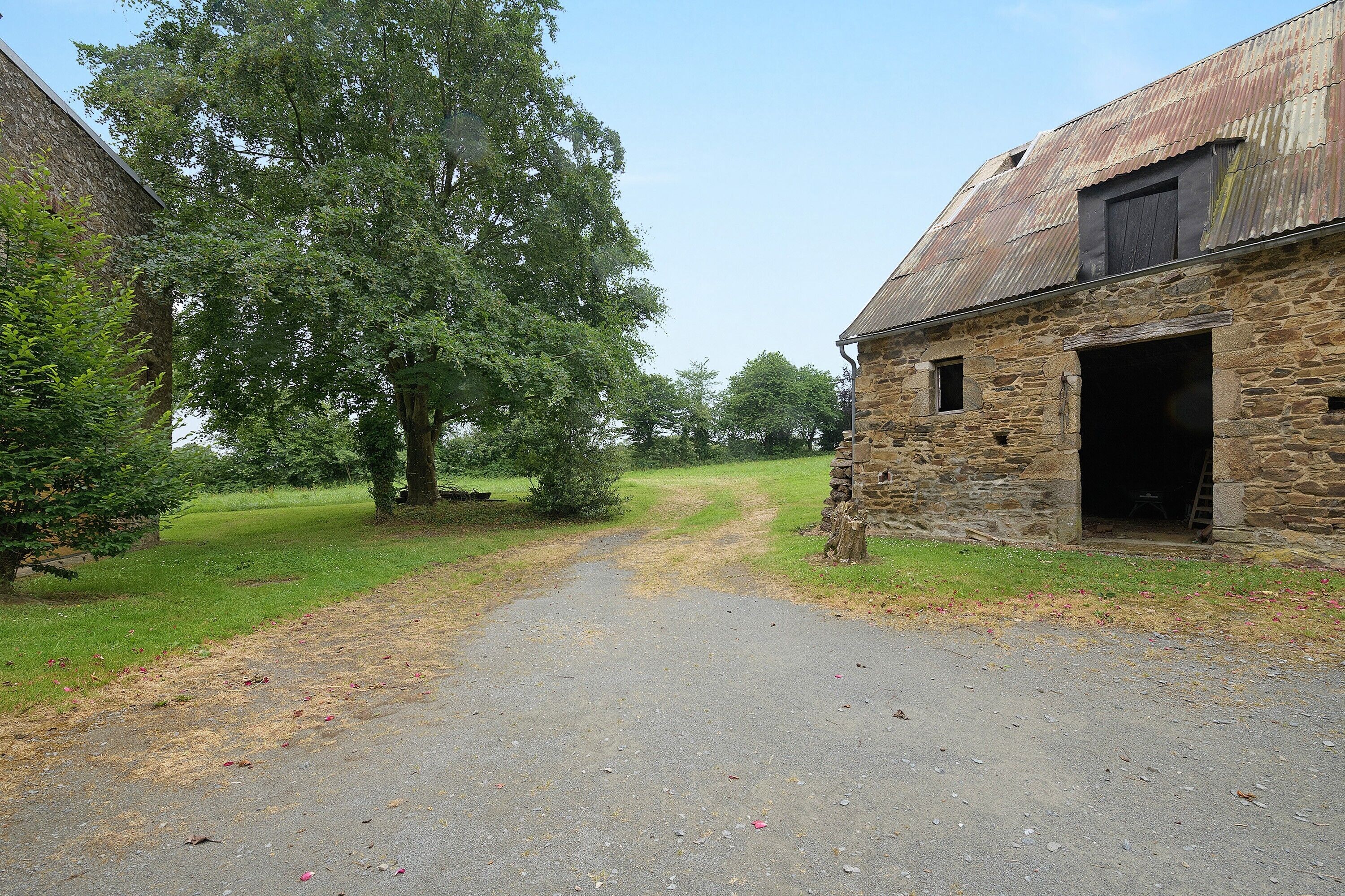A rural stone building with a dirt path leading to it, surrounded by trees and open fields.