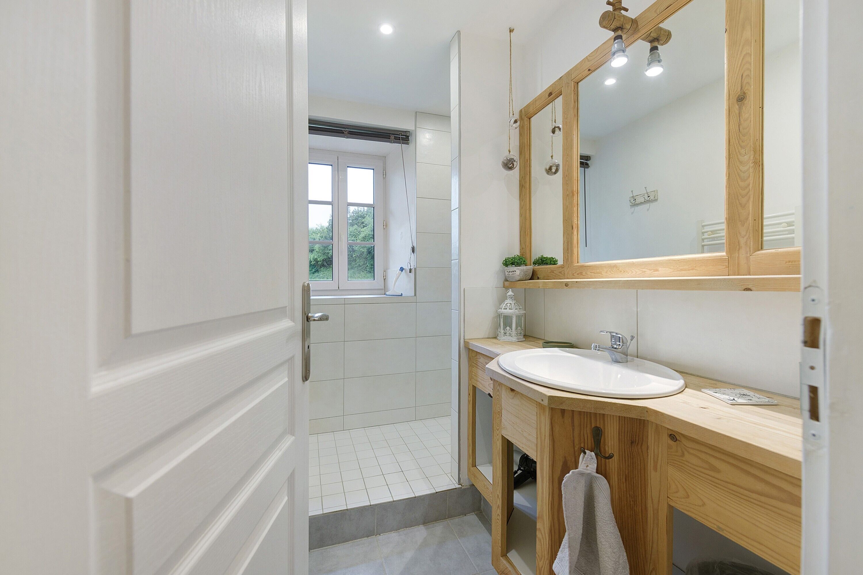 A modern bathroom with a white sink, wooden vanity, and a large mirror.