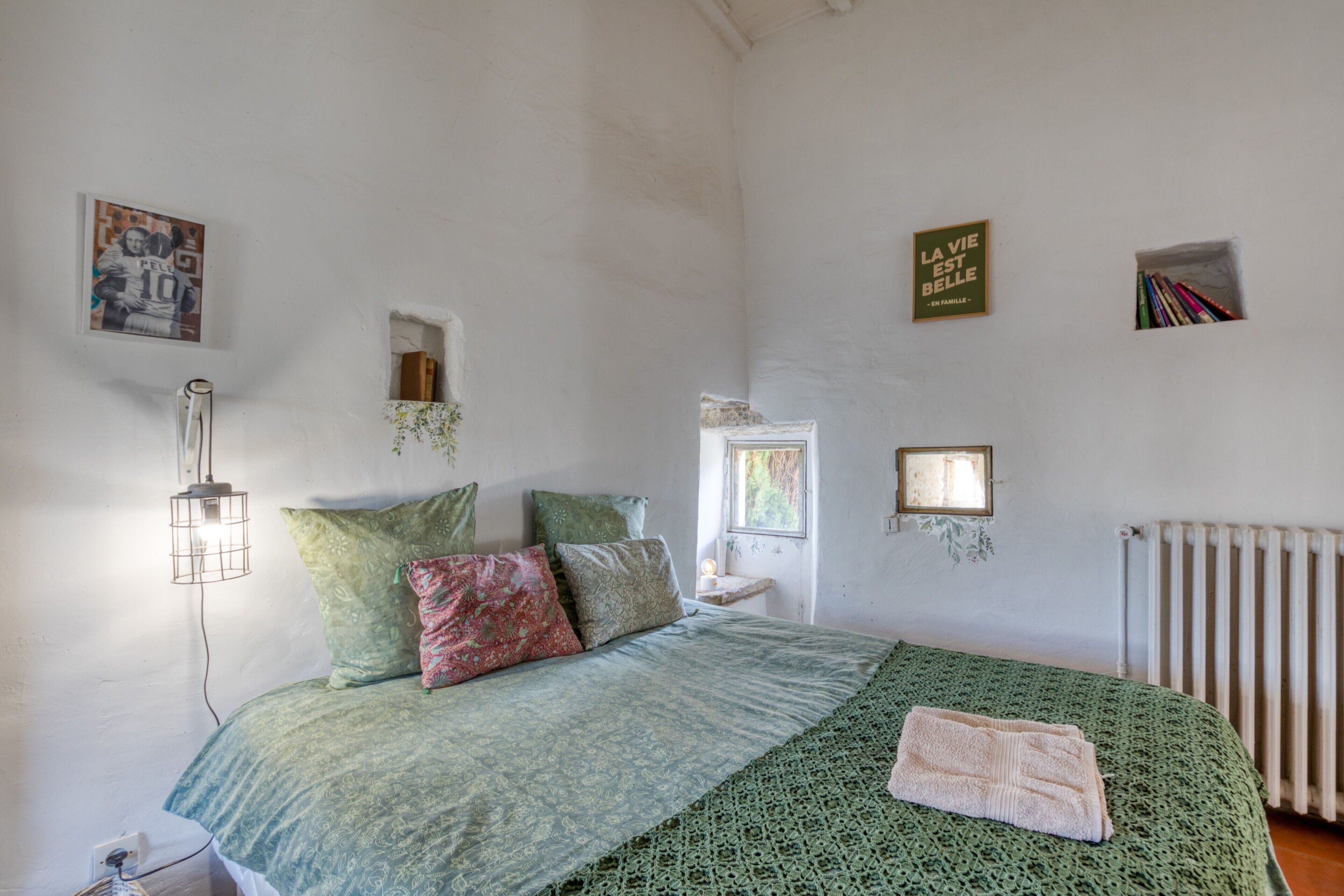 Une chambre à coucher avec un lit, des oreillers, une lampe de chevet, un radiateur et des éléments décoratifs sur les murs.