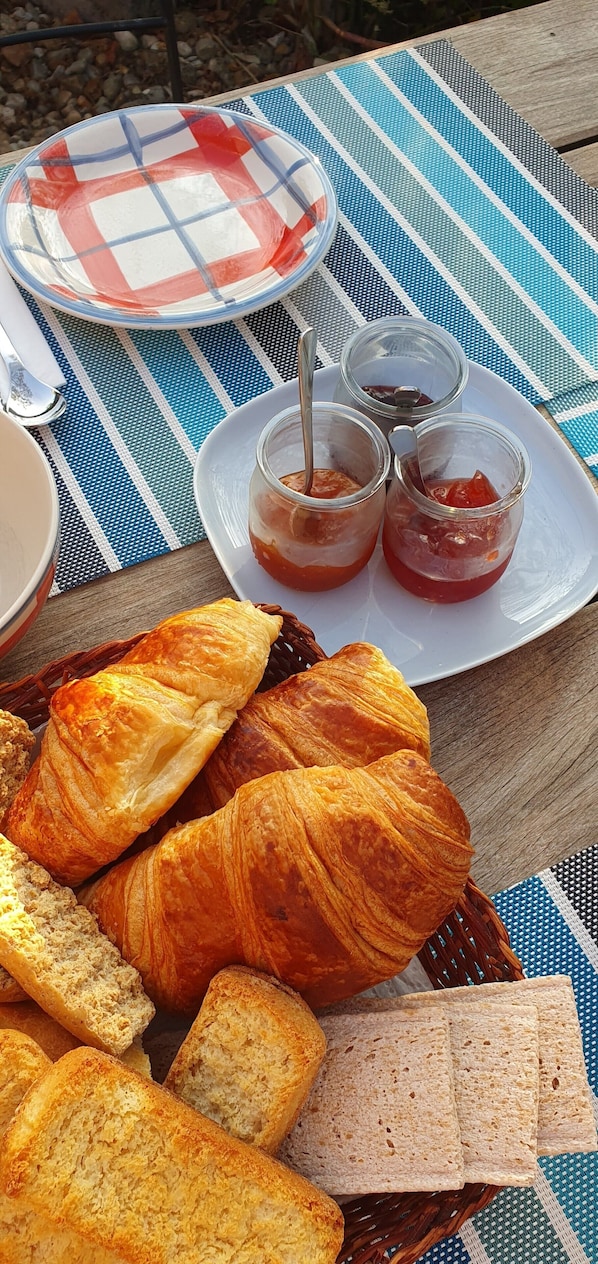 A picnic setup with croissants, bread, and jam on a striped tablecloth.