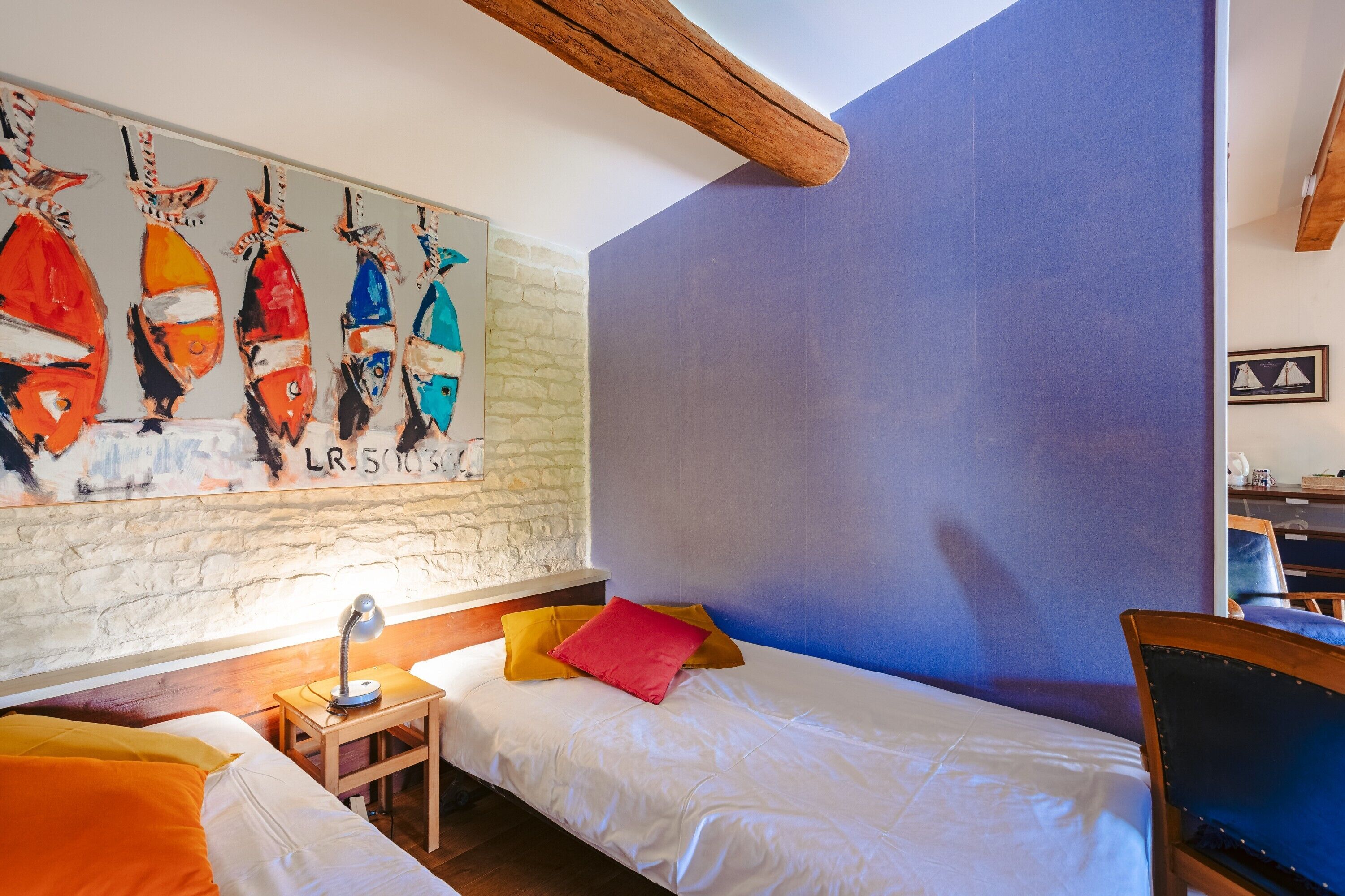 Une chambre avec deux lits, une tête de lit en bois, un mur en pierre et un tableau représentant des bateaux.