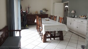 Un espace repas comprenant une table, des chaises, un ventilateur de plafond, ainsi qu’un coin cuisine avec des placards et un plan de travail.