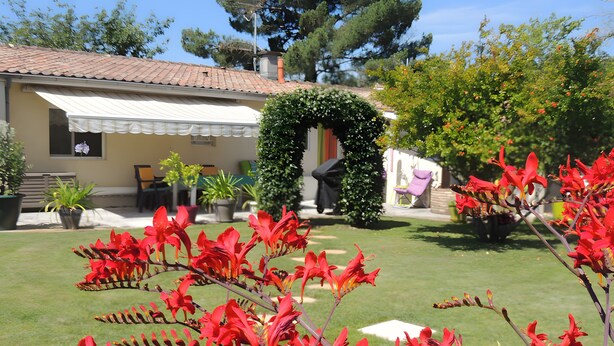 Un jardin avec des fleurs rouges, un bâtiment blanc avec un toit en tuiles et une pelouse verte.