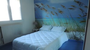 Un lit avec une literie blanche dans une chambre dont un des murs est décoré d’une fresque représentant une plage.