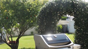 Un barbecue extérieur doté de commandes, installé sur un gazon bien entretenu, avec des arbres en arrière-plan.