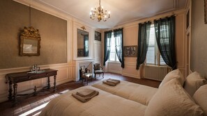 Una habitación con dos camas, un escritorio de madera, una silla, una chimenea y un ventanal con cortinas.