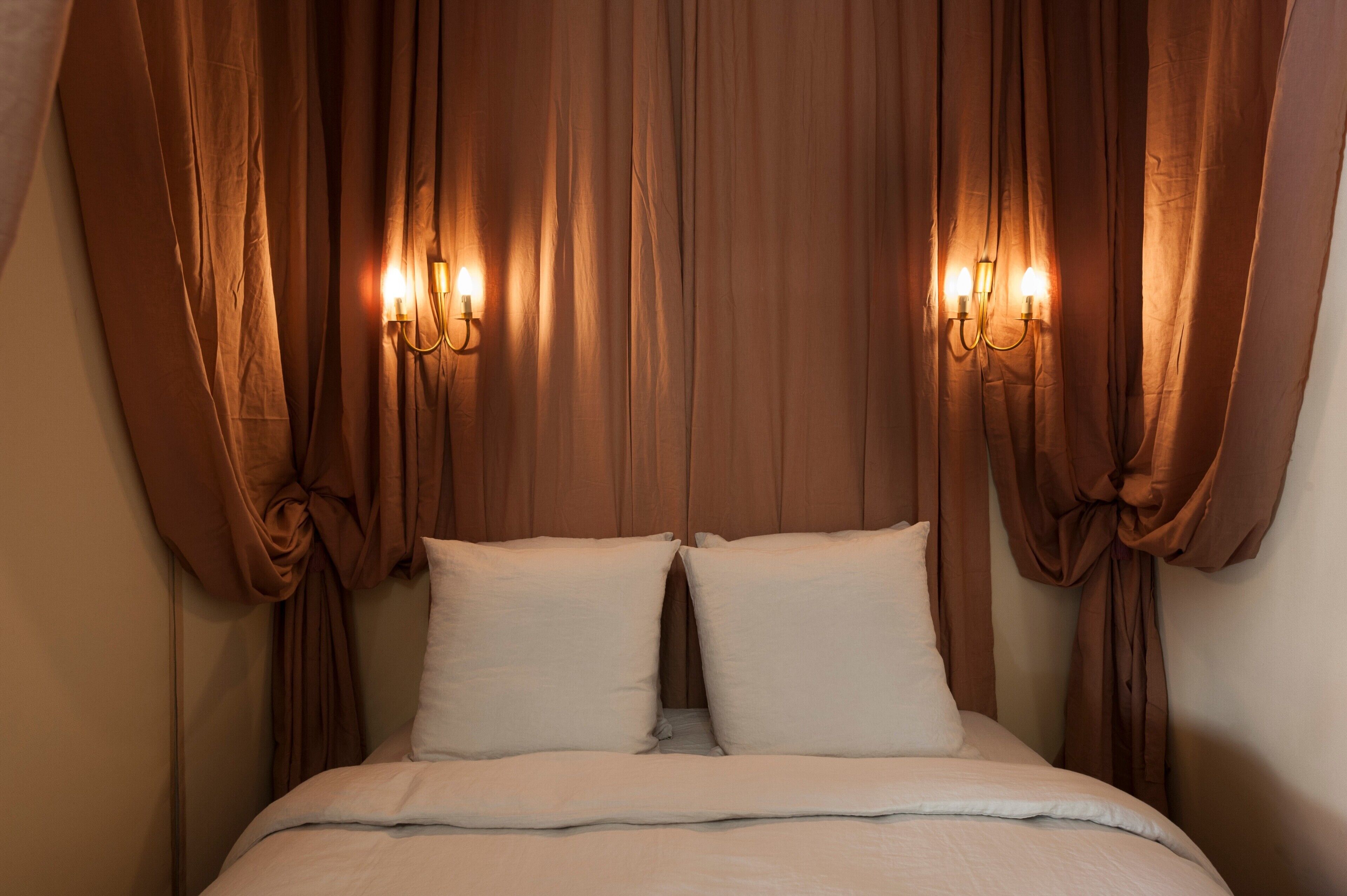 Un lit avec du linge de lit blanc, des rideaux marron et des appliques murales.