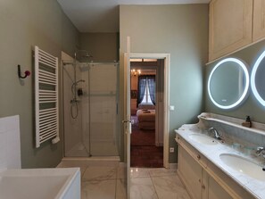 Un baño con bañera, ducha, tocador con dos lavabos y espejo con luz.
