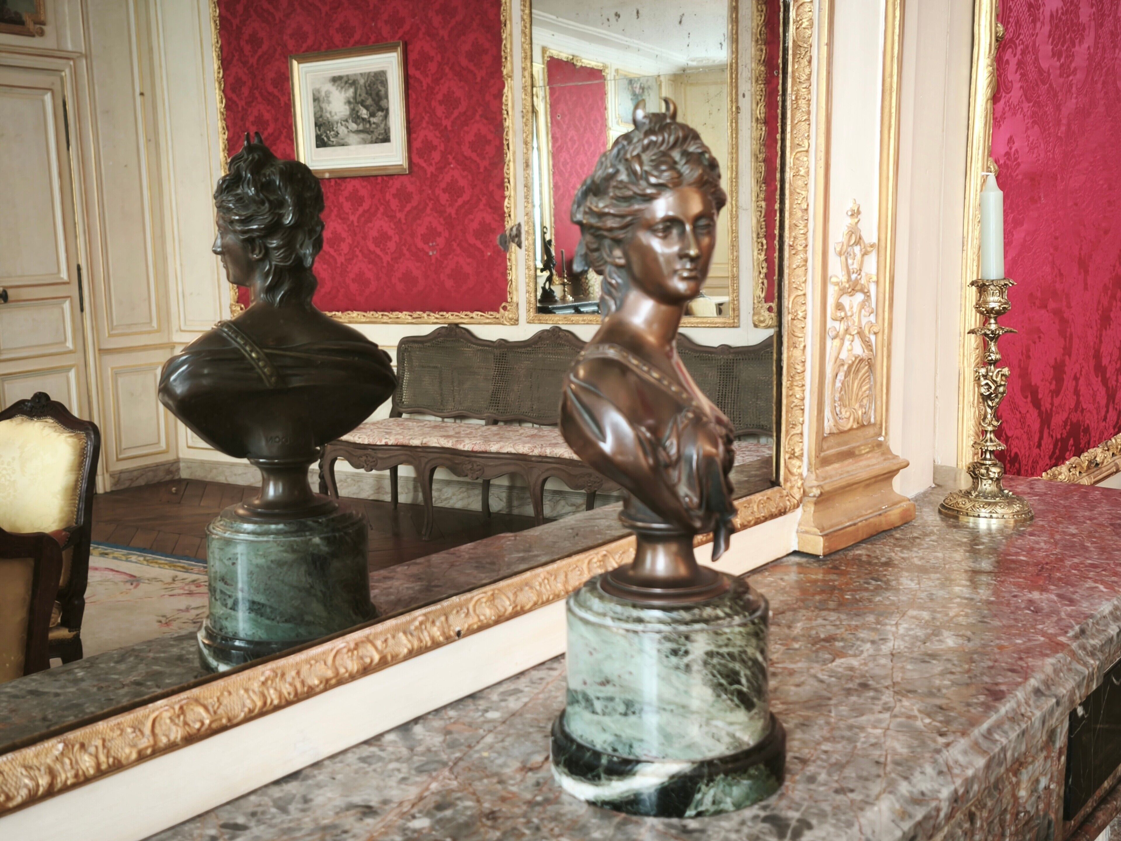 A marble countertop with a bust sculpture, a mirror, and a decorative candle holder.