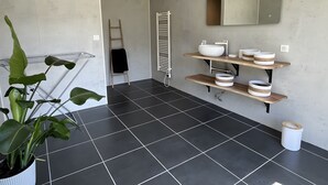 Een moderne badkamer met zwarte tegels, een grote spiegel en planken met toiletartikelen.