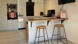 Een moderne keuken met een centraal eiland, barstoelen, een magnetron, oven en een flatscreen televisie aan de muur.