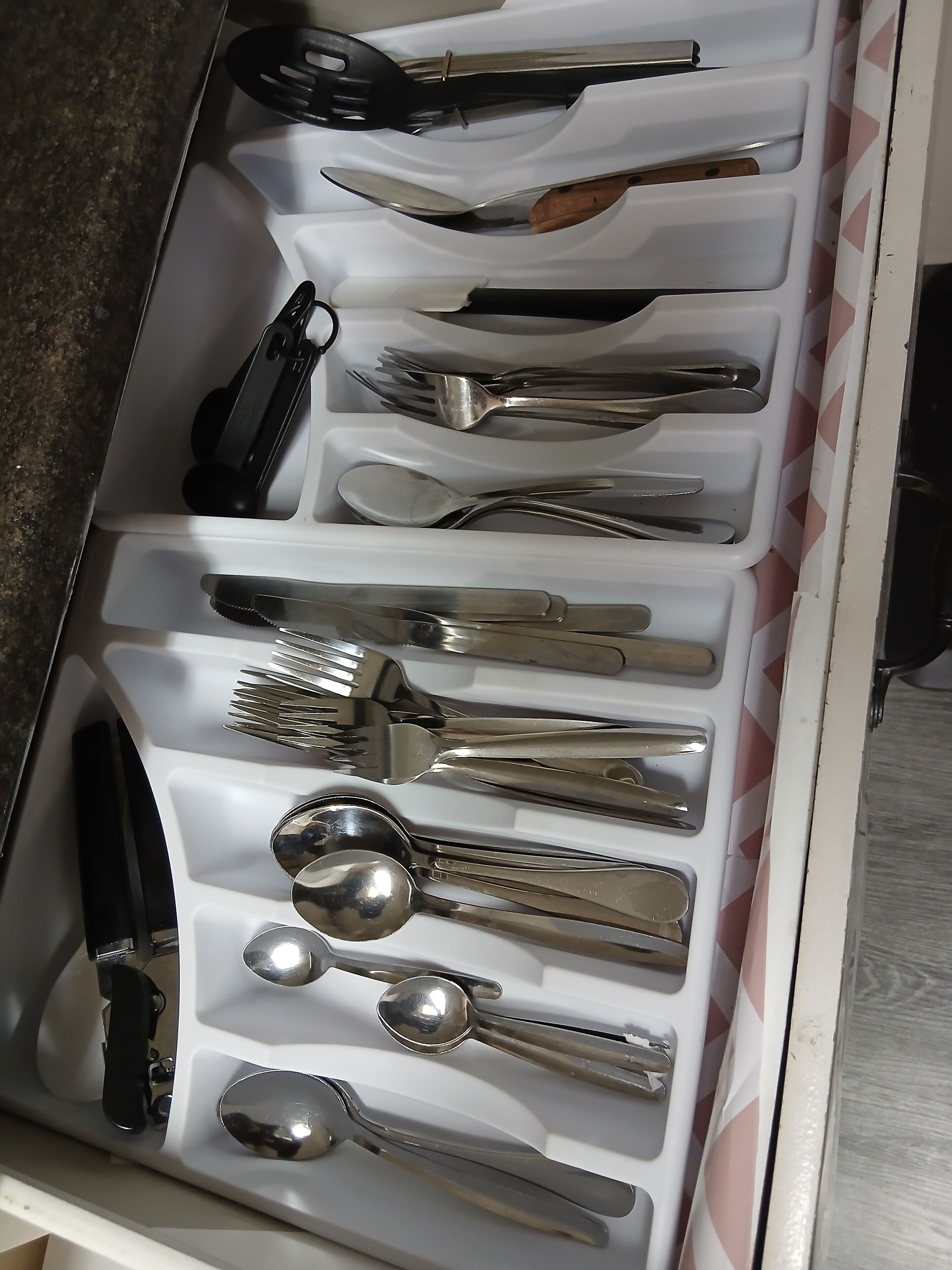 Un cajón con diversos utensilios de cocina, incluyendo cuchillos, cucharas, tenedores y un rallador.