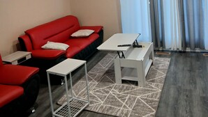 En moderne stue med en rød sofa, to hvide borde, et mønstret tæppe og en loftlampe.