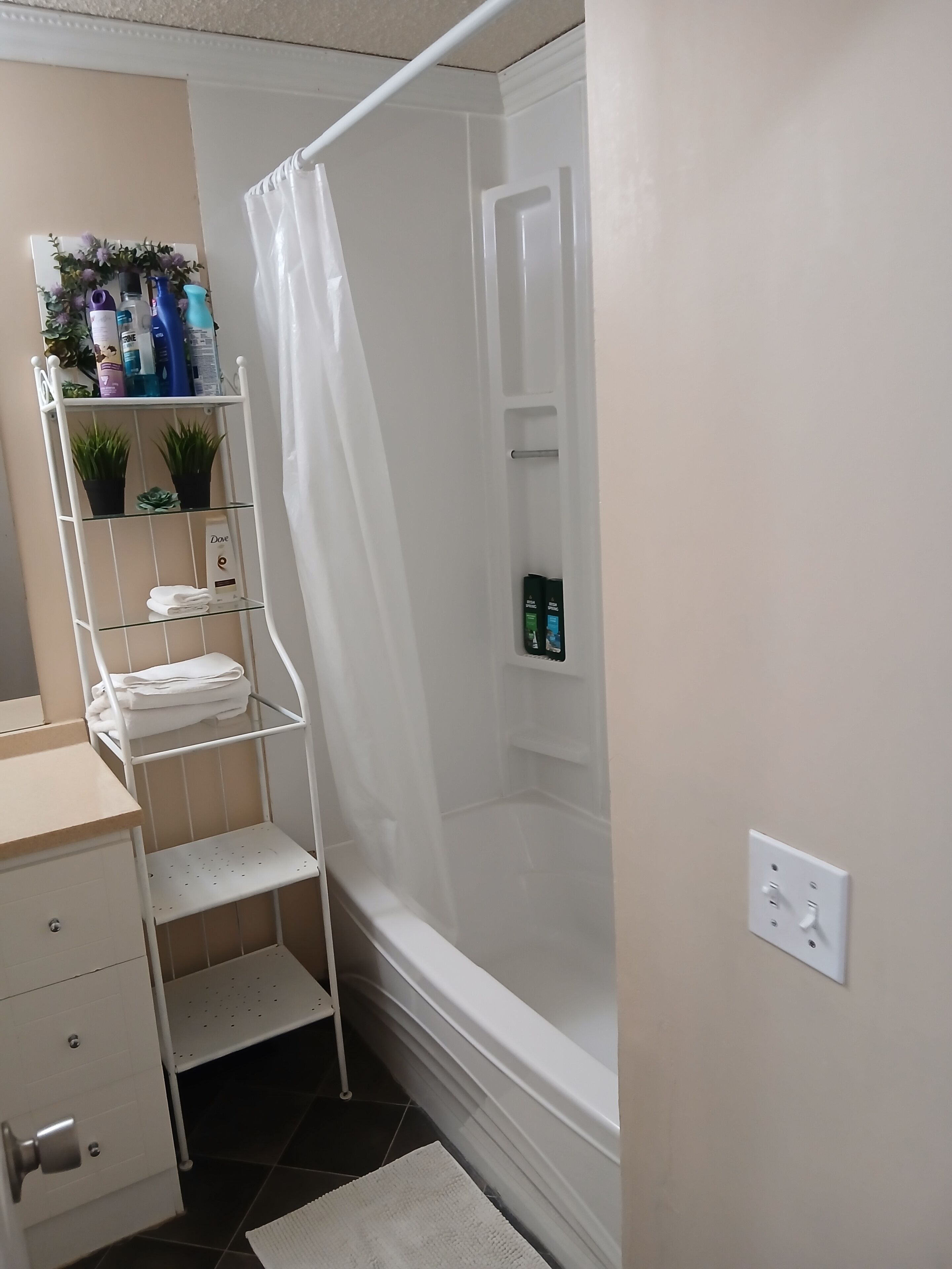Een badkamer met een douche, een wit schap met toiletartikelen en een handdoekrek.