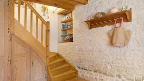 Una escalera de madera que lleva a una habitación con paredes de piedra, un estante con sombreros y un bolso colgado en la pared.
