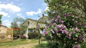 Una casa de piedra rústica con jardín, flores moradas y valla de madera.