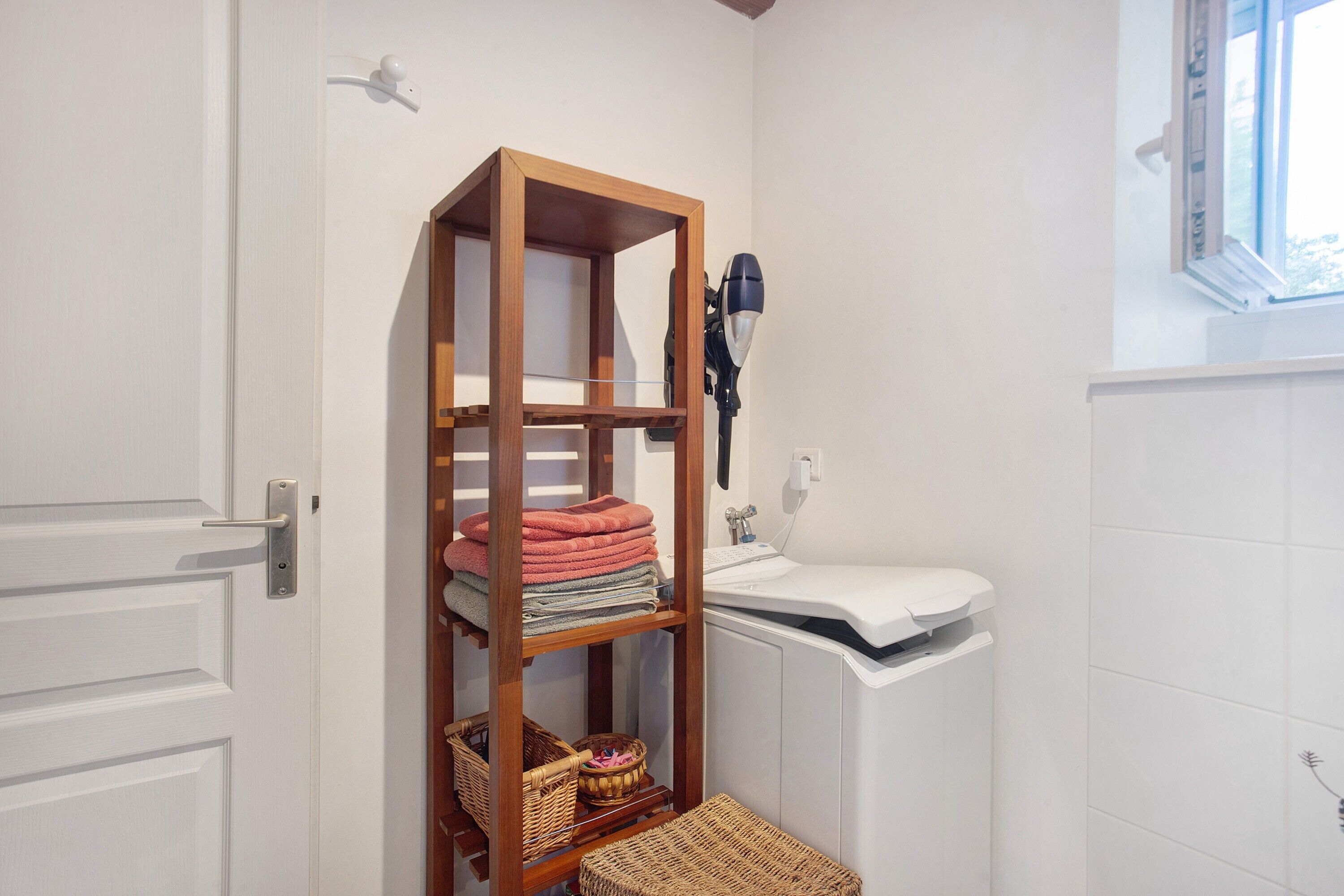 A bathroom with a wooden shelf, a hairdryer, a sink, and a window.
