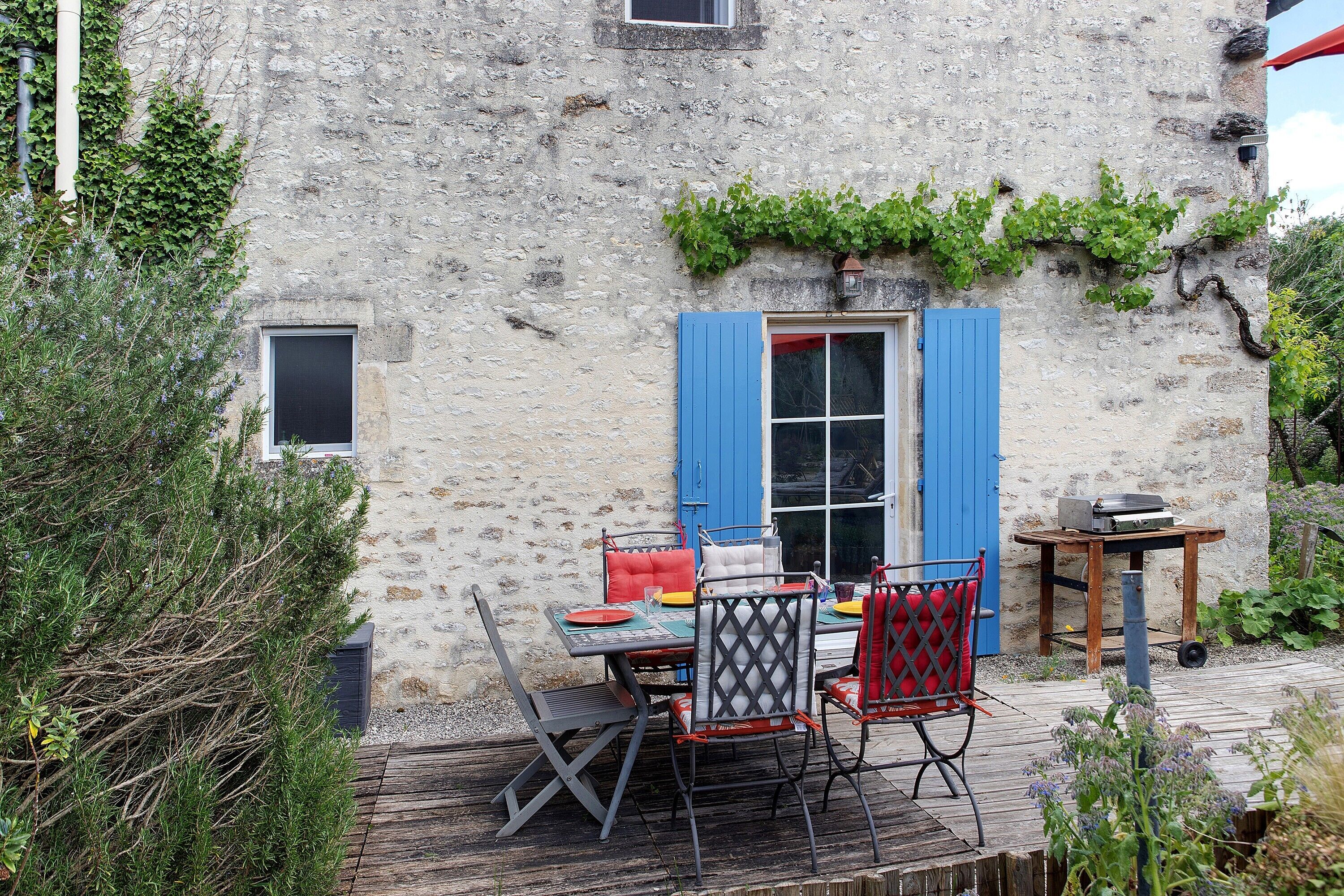 Un comedor al aire libre rústico con una mesa y sillas, una mesita con un radio, y una terraza de madera.